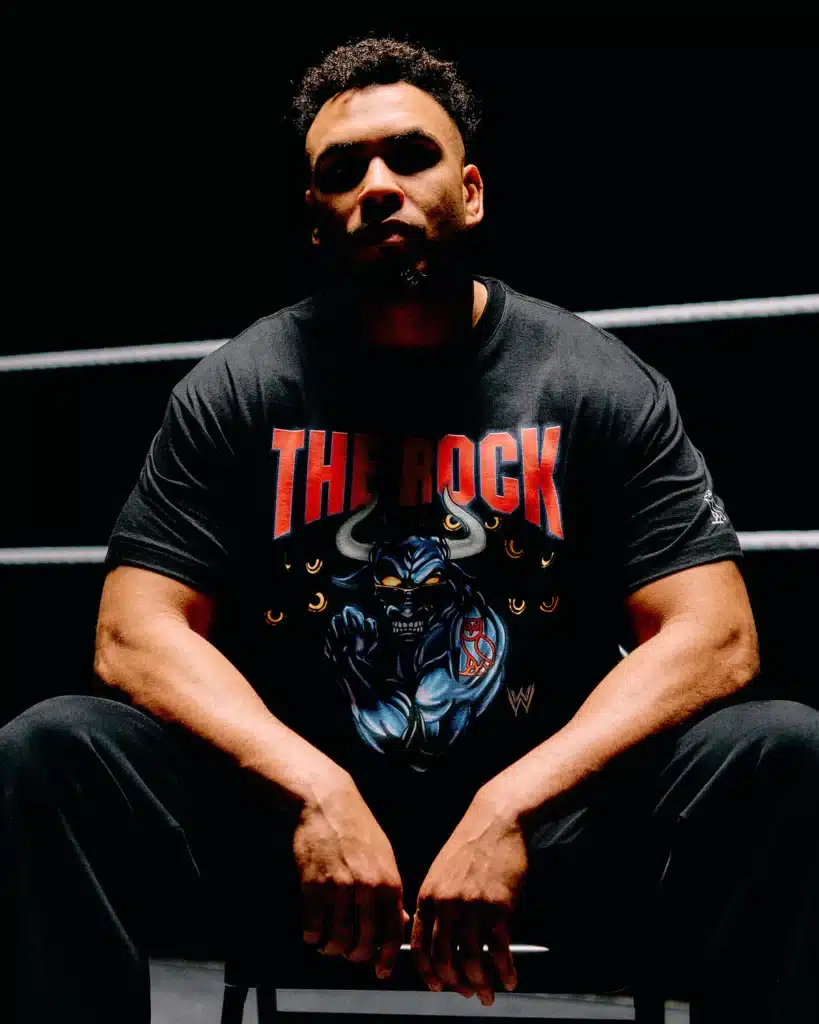 OVO x WWE: A person sitting in a dark room wearing a black T-shirt with a graphic and the text "The Rock."