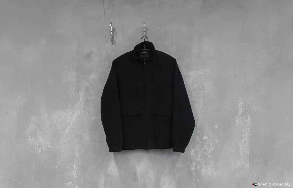 A black jacket hanging on a hanger against a textured gray wall.