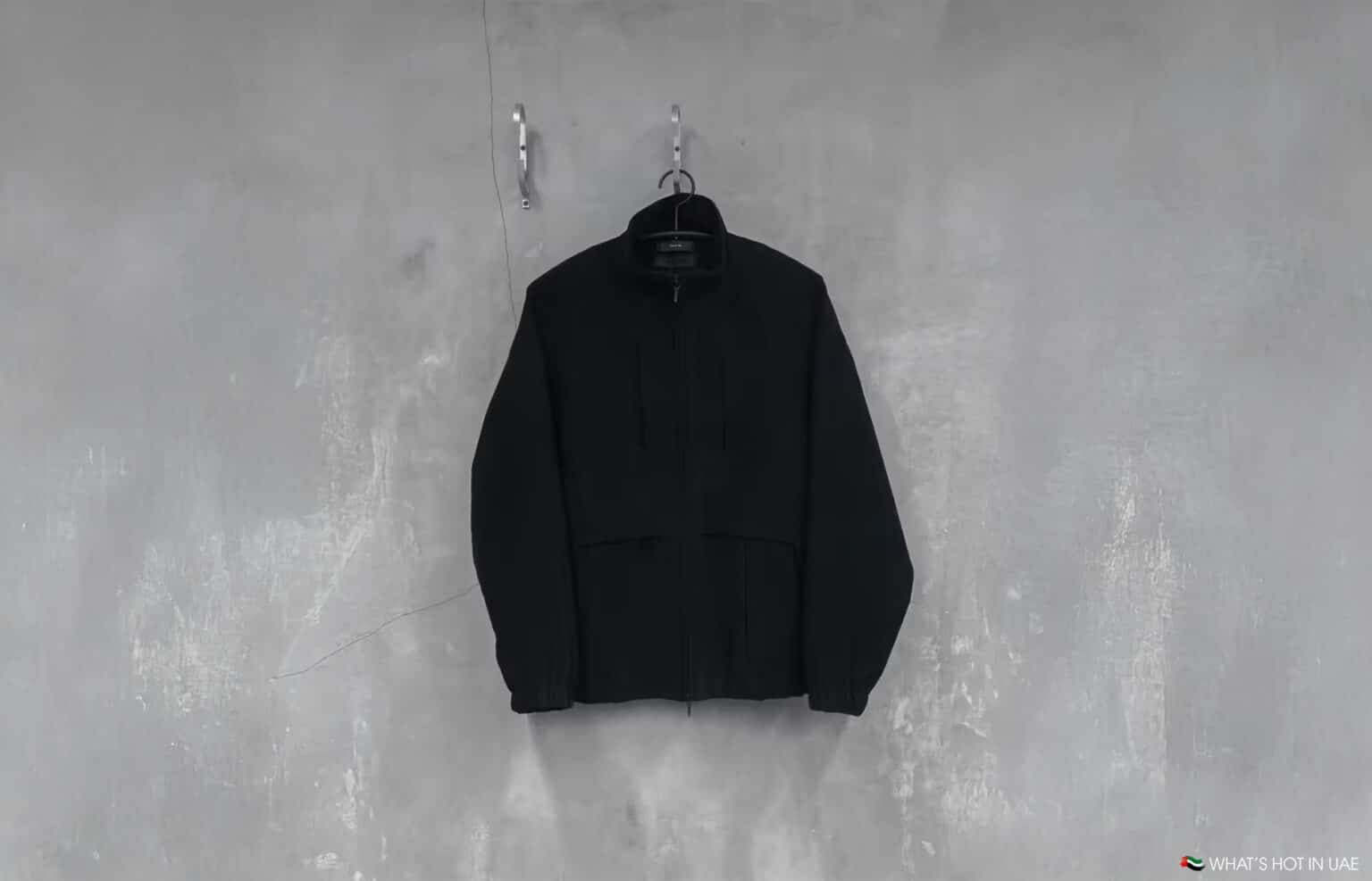 A black jacket hanging on a hanger against a textured gray wall.