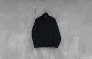 A black jacket hanging on a hanger against a textured gray wall.