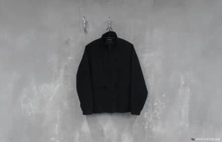 A black jacket hanging on a hanger against a textured gray wall.