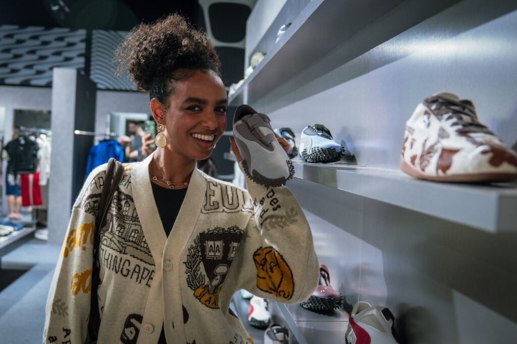 A person smiling and holding a shoe in the Puma Lounge Dubai, with various Puma sneakers displayed on shelves.