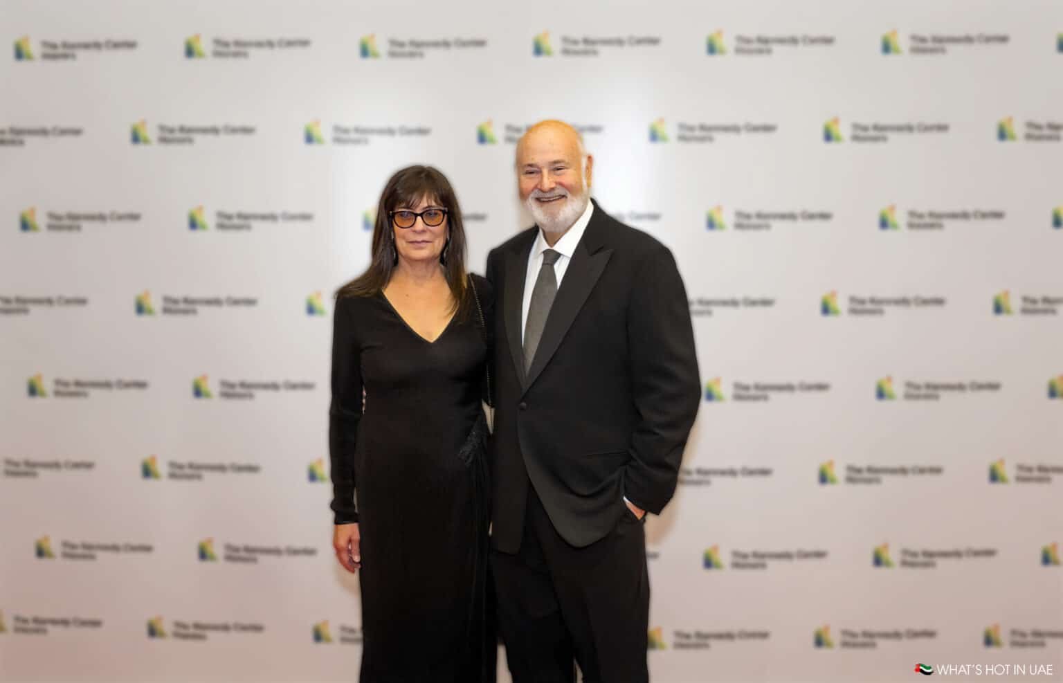 A man and a woman dressed formally, posing together on a red carpet with a backdrop labeled 'The Kennedy Center Honors.'