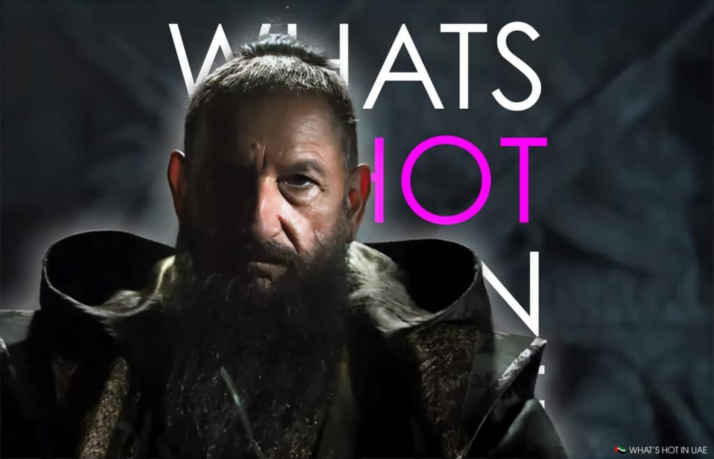 A serious-looking man with a long beard, wearing a dark coat, with bold text in the background reading "WHAT'S HOT."