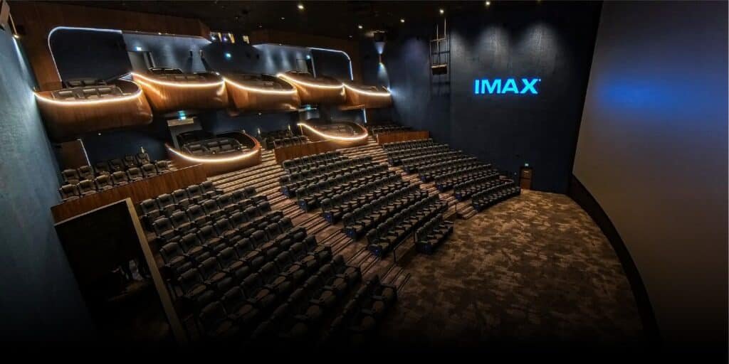 A large, dimly lit IMAX theater with rows of empty seats and illuminated balcony seating.