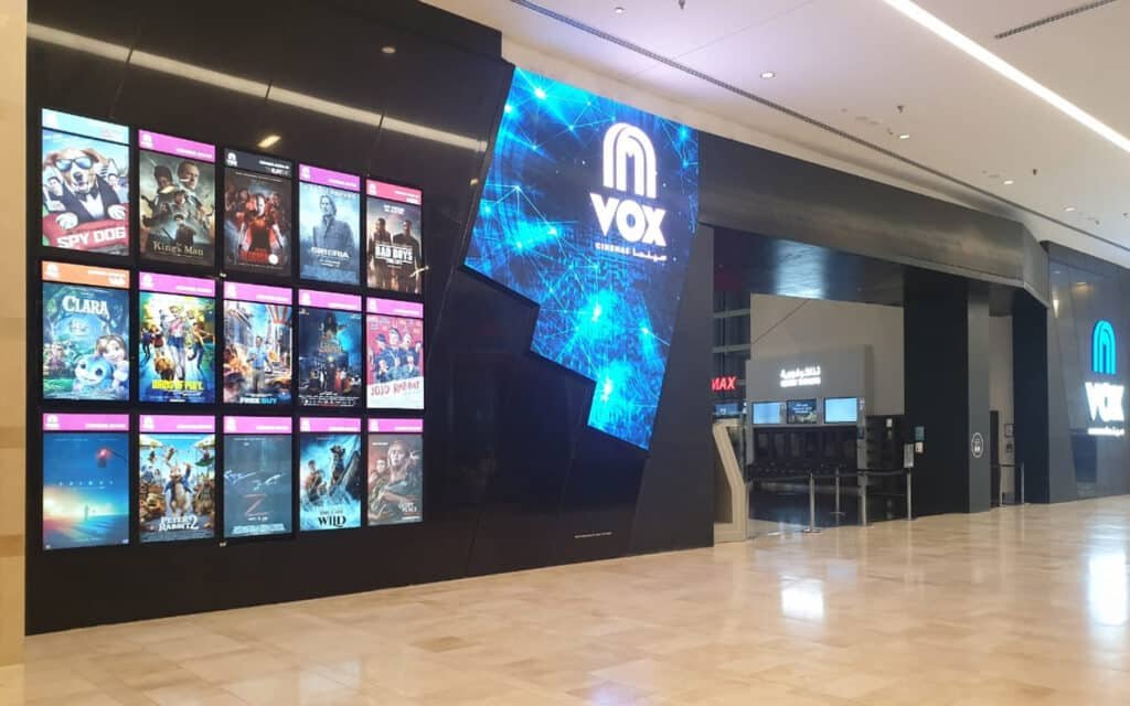 A IMAX Yas Mall movie theater entrance with posters of various films and a large illuminated VOX sign.