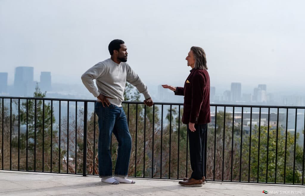 Wonder Man & Trevor stand on a terrace with a city skyline in the background, engaged in conversation.