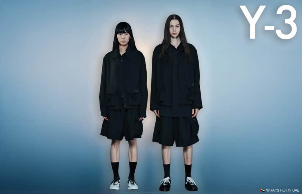 Two models standing against a blue background, both wearing oversized black jackets and shorts with black socks; accompanied by the text 'Y-3' on the top right corner.