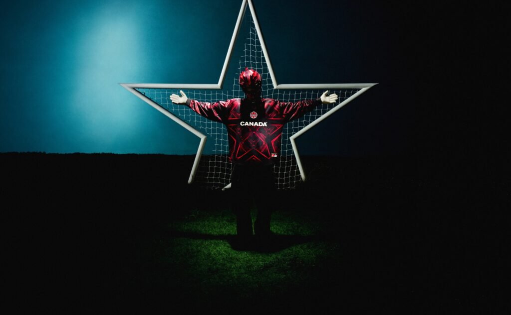 A person wearing a red Canadian hockey jersey and a helmet stands with arms outstretched in front of a star-shaped frame and net, set against a dark background with a gradient of blue and black.
