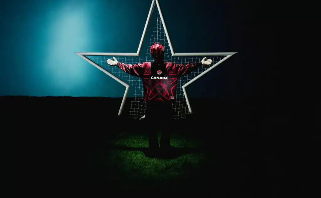 A person wearing a red Canadian hockey jersey and a helmet stands with arms outstretched in front of a star-shaped frame and net, set against a dark background with a gradient of blue and black.