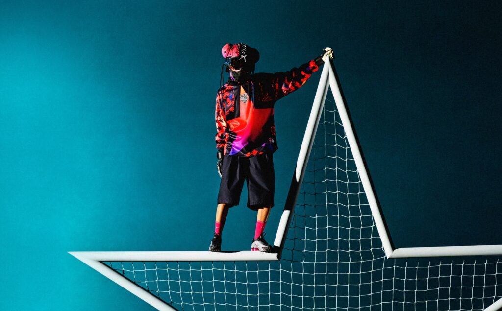 Nike Hollywood Keepers: A person wearing a colorful jacket and mask stands on a large star-shaped goal net, set against a blue background.