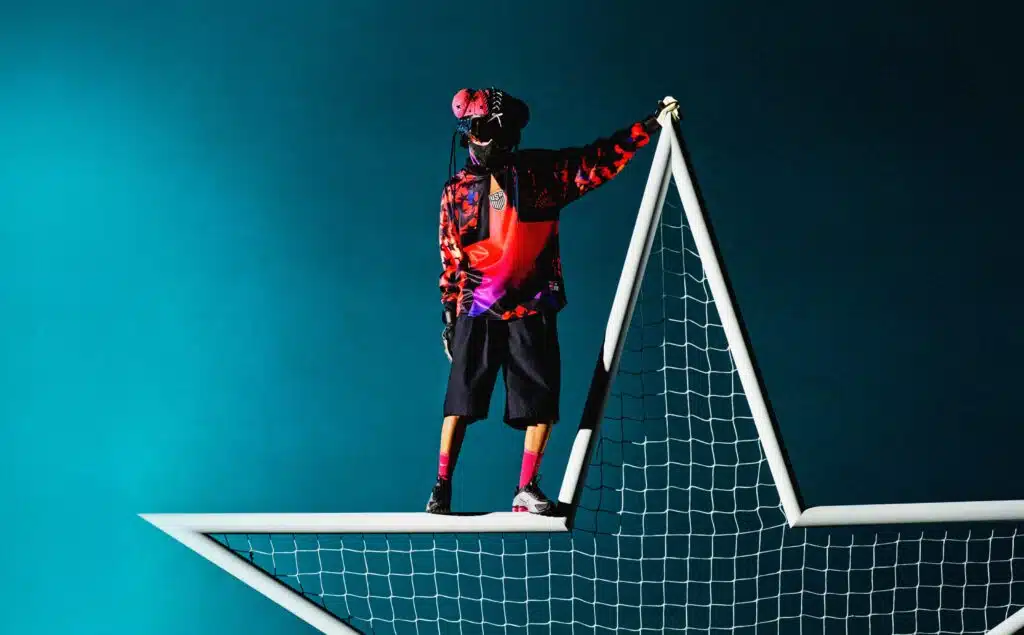 Nike Hollywood Keepers: A person wearing a colorful jacket and mask stands on a large star-shaped goal net, set against a blue background.
