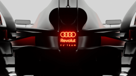 Rear view of a sleek Formula 1 car displaying the logos "Revolut" and "F1 Team" with an illuminated red logo above.