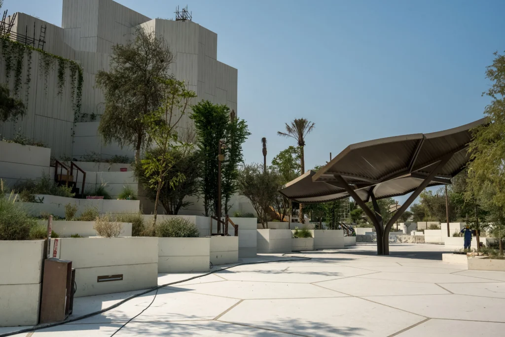  Abu Dhabi Natural History Museum outdoor plaza with geometric landscaping, featuring tiered planters, various trees, and a large angular canopy.