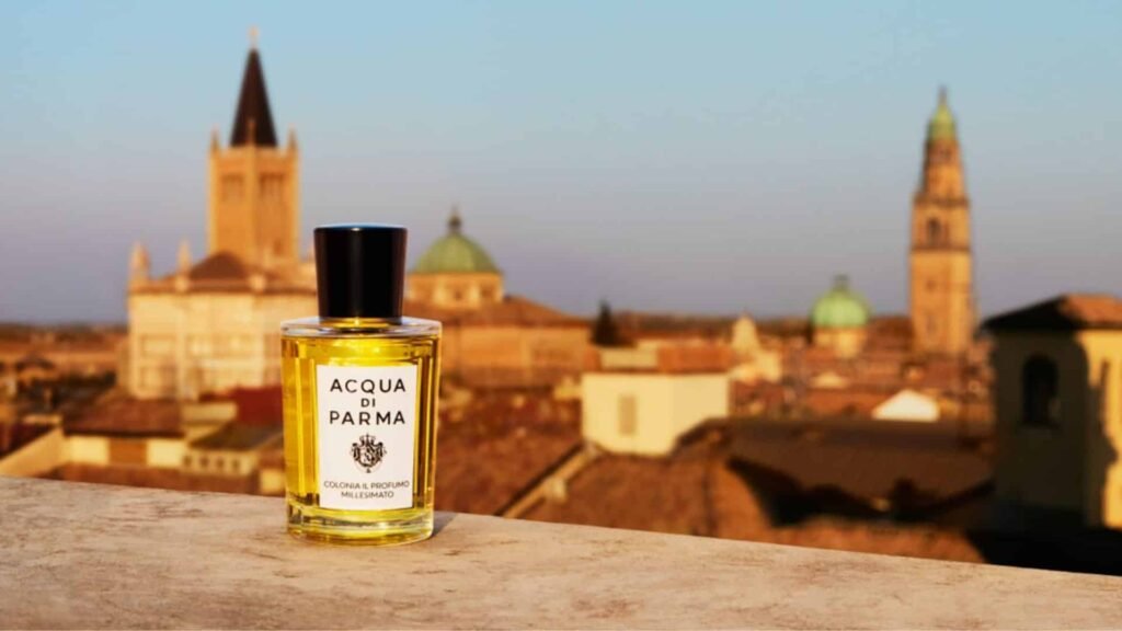 A bottle of fragrance on a ledge with a blurred cityscape featuring historic towers in the background.