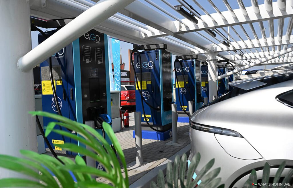 Electric car Adnoc E11 EV charging station with multiple blue E-GO chargers under a canopy, and a silver vehicle partially visible.