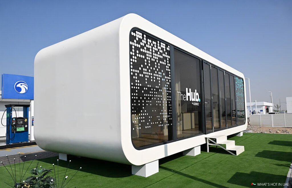 Rectangular, futuristic Adnoc E11 EV building labeled "The Hub," featuring a large QR code design on the side, set outdoors.