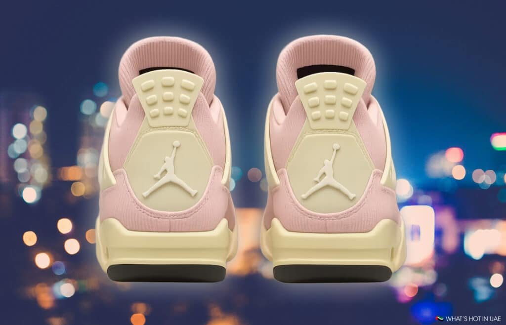 Two pink Air Jordan 4 'Iced Carmine' sneakers with white soles and a white logo against a blurred city lights background.