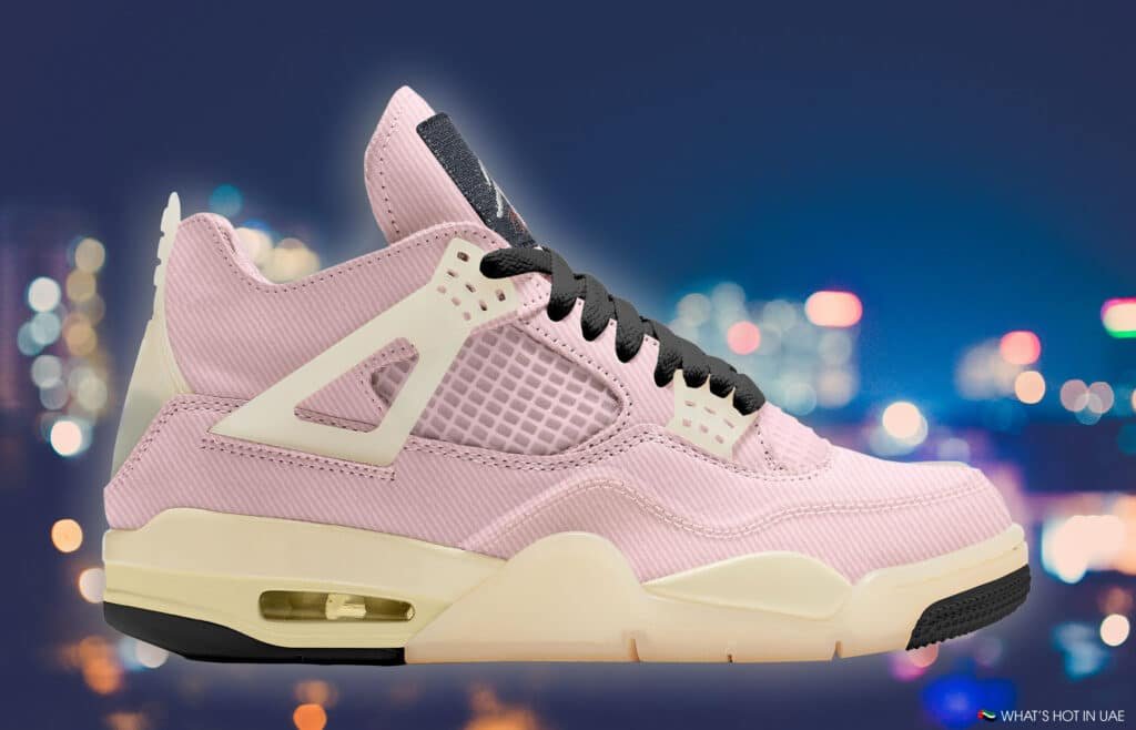 A pink sneaker with white and black accents, featuring a visible air unit, against a blurred cityscape background.