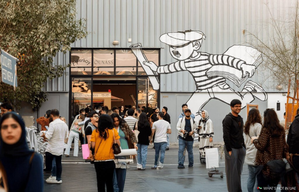 Visitors entering a gallery space at Al Quoz Arts Fest, framed by a large illustrated mural on a warehouse wall and crowds exploring the arts district.