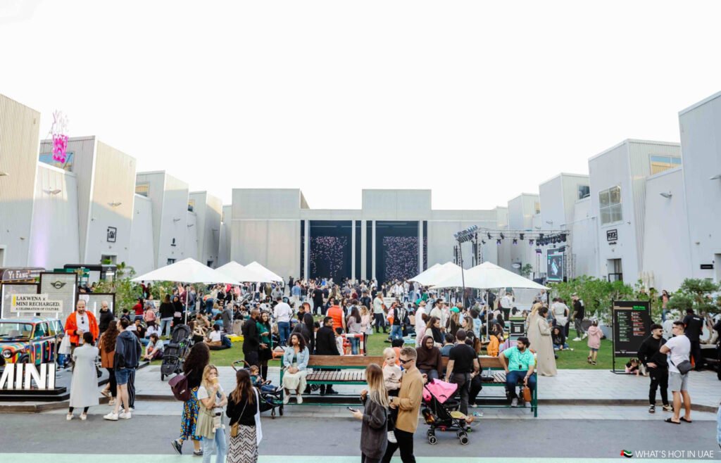 Families and visitors relaxing in the central courtyard at Al Quoz Arts Fest, with outdoor seating, pop-up stalls, and live cultural activities.