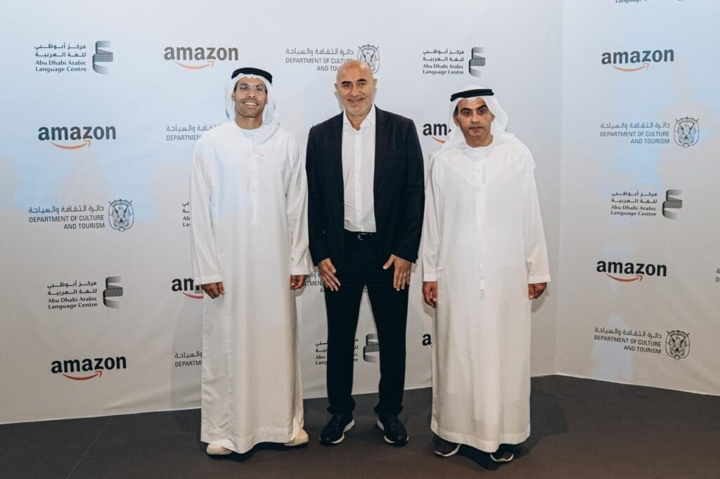 Three people standing in front of a promotional wall to promote Amazon Digital Arabic Library partnership with Abu Dhabi Literature.