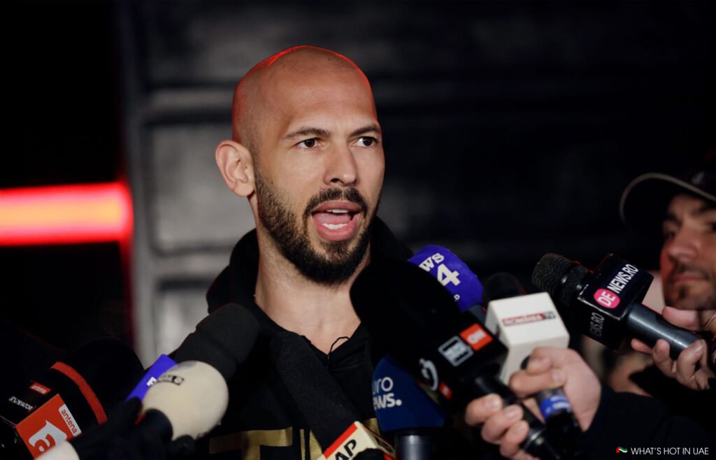 Andrew Tate with a shaved head speaks into multiple microphones at a press event.