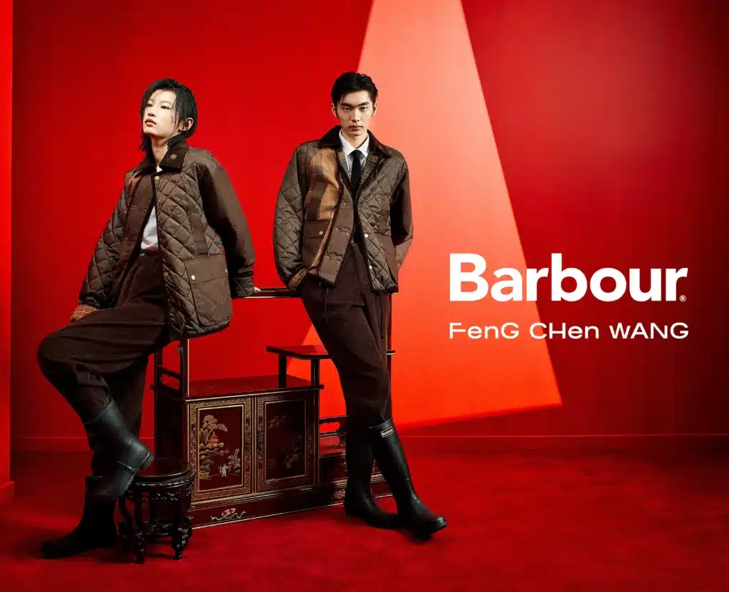 Two models in Barbour and Feng Chen Wang clothing pose against a bold red backdrop, with jackets and boots.