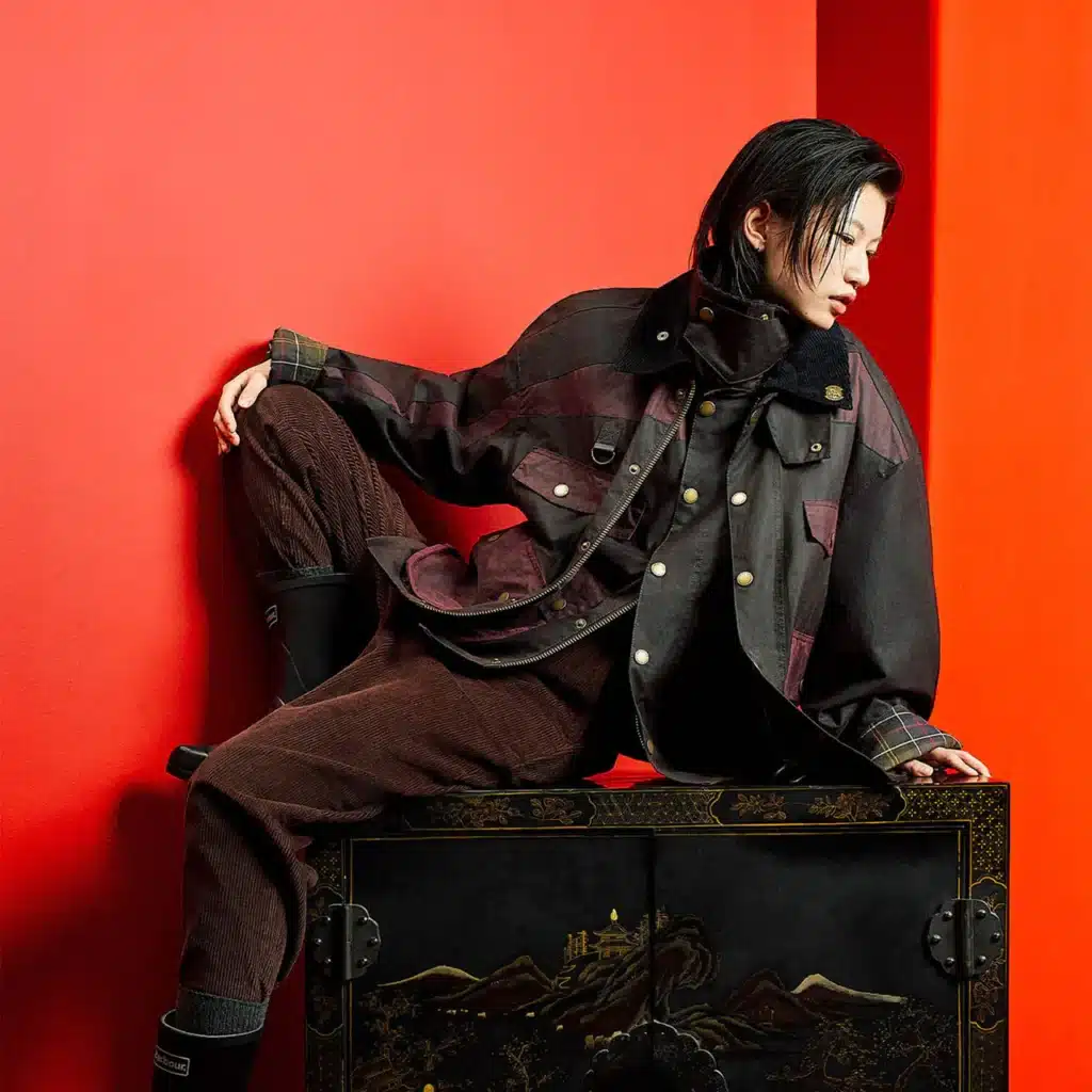 Person in stylish layered clothing leans against a decorative cabinet with a bold red background.