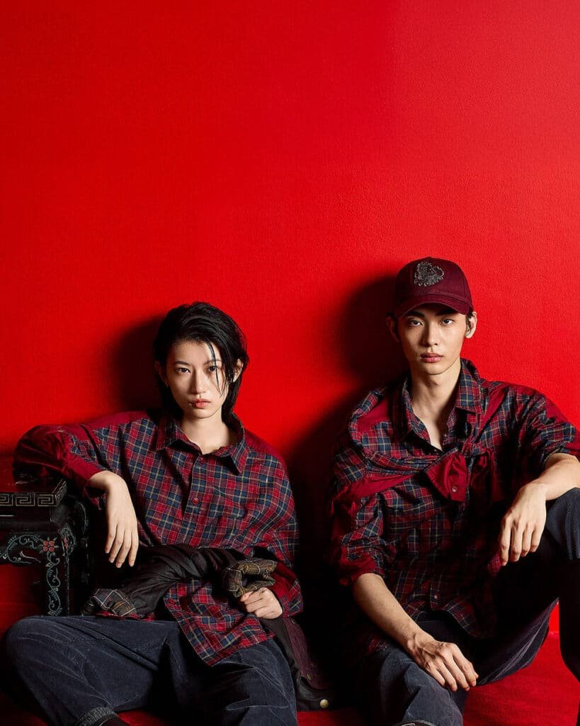 Two people wearing matching red plaid shirts sit against a vibrant red background.