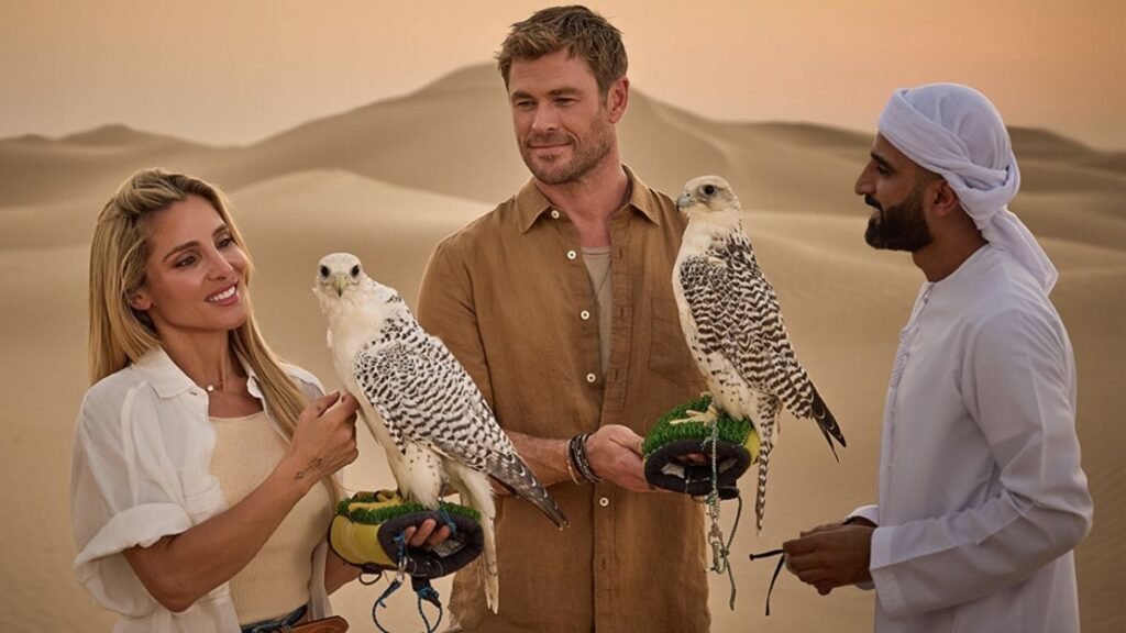 Chris Hemsworth in a desert holding falcons, with sand dunes in the background.