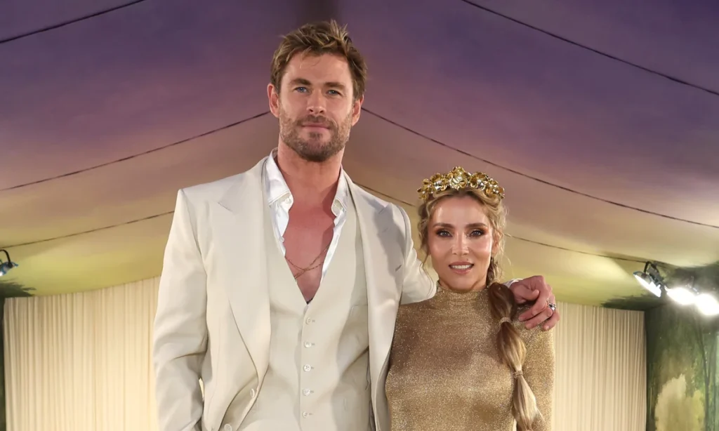 A couple posing together; the man wears a white suit, and the woman wears a gold dress with a floral headpiece.