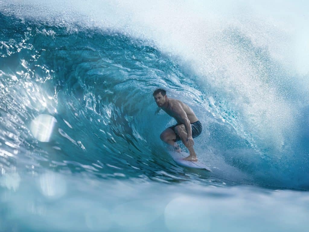 Chris Hemsworth rides inside a large, translucent blue wave.