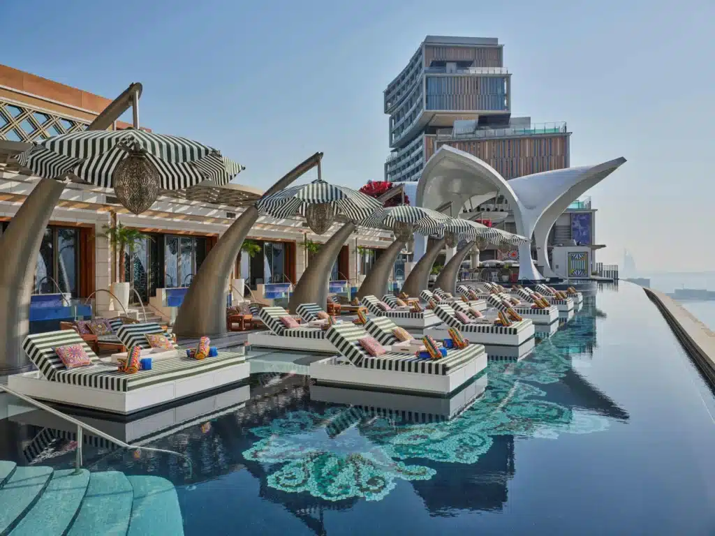 Best Pools & Pool Bars in Dubai: Poolside lounge area with striped umbrellas, cushioned seating, and a modern architectural backdrop.