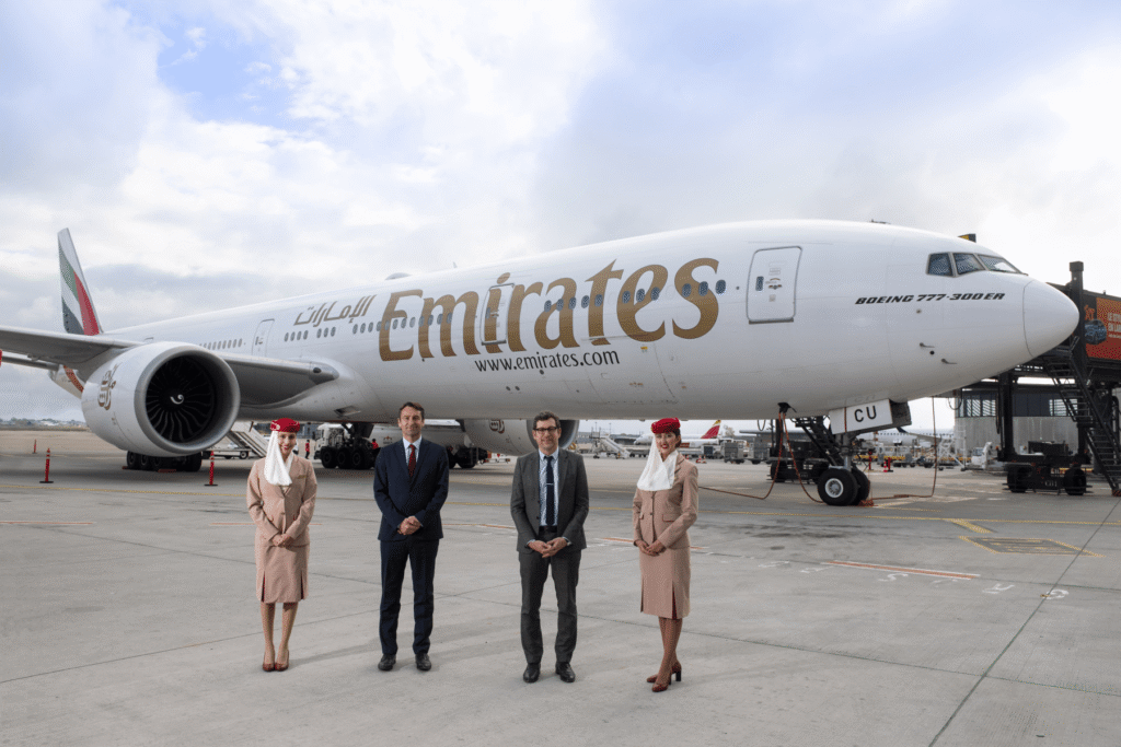 Emirates Boeing 777 aircraft on the runway with cabin crew and officials standing in front during a formal aviation presentation.