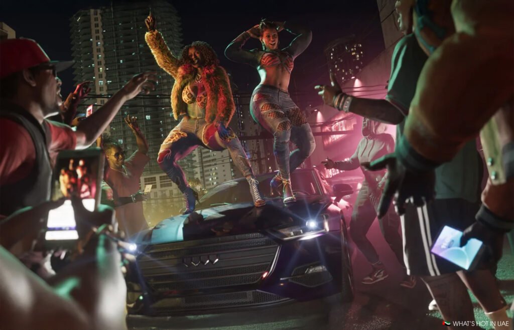 Two people energetically dancing on a car hood at night, surrounded by a crowd taking photos with phones.