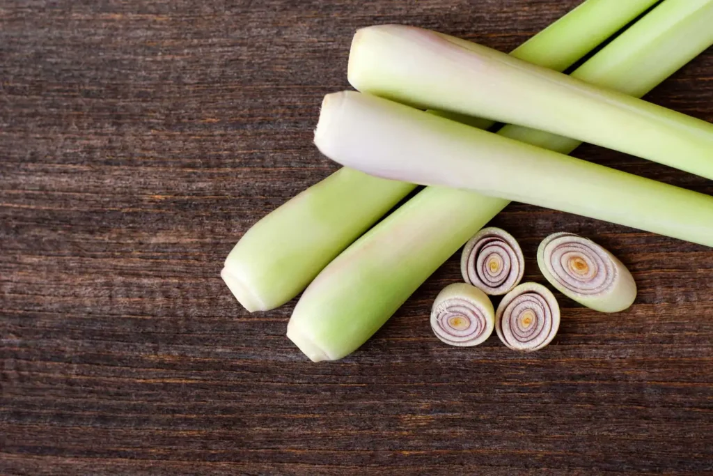 Fresh Lemongrass Cancer Research stalks and slices on a dark wooden surface.