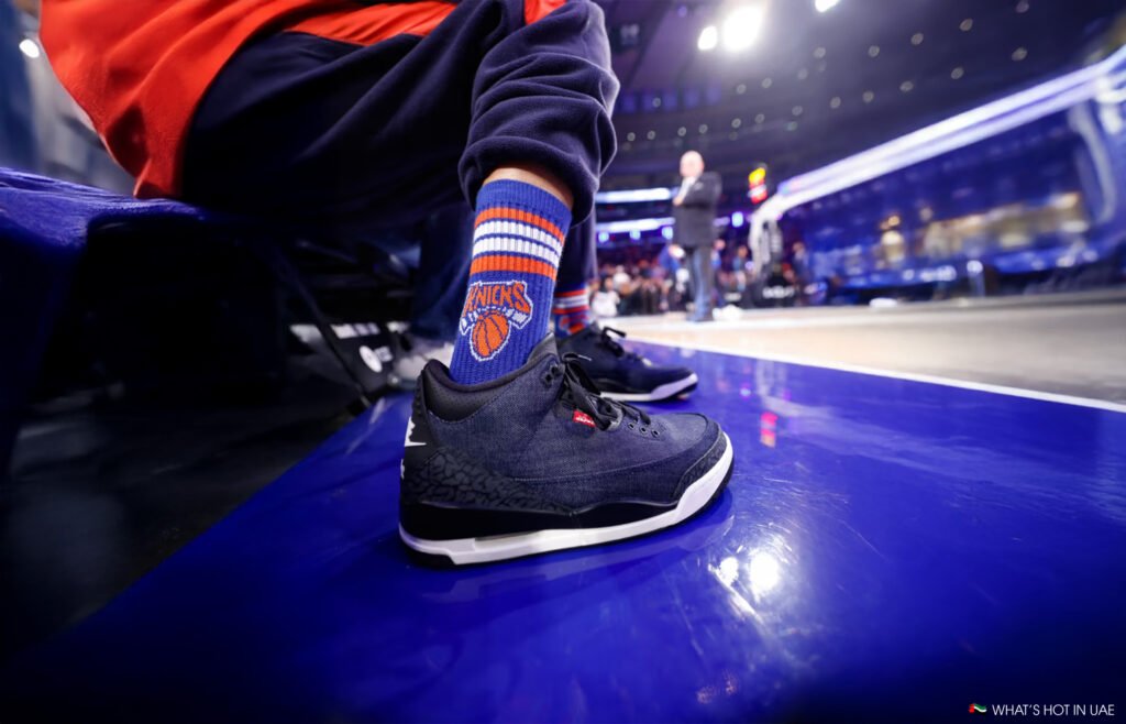 A person wearing dark blue sneakers with basketball-themed socks sits on a bench in a brightly lit indoor arena.