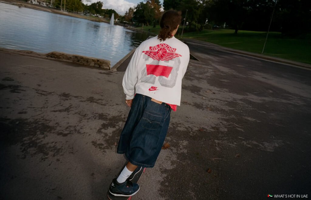 Person skateboarding near a lake, wearing a jacket with a large Levi's x Jordan Brand logo and baggy denim shorts.