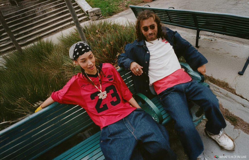 Two people sitting on a green bench, both wearing casual Levi's x Jordan Brand denim and red clothing; one wears a bandana and a large necklace.