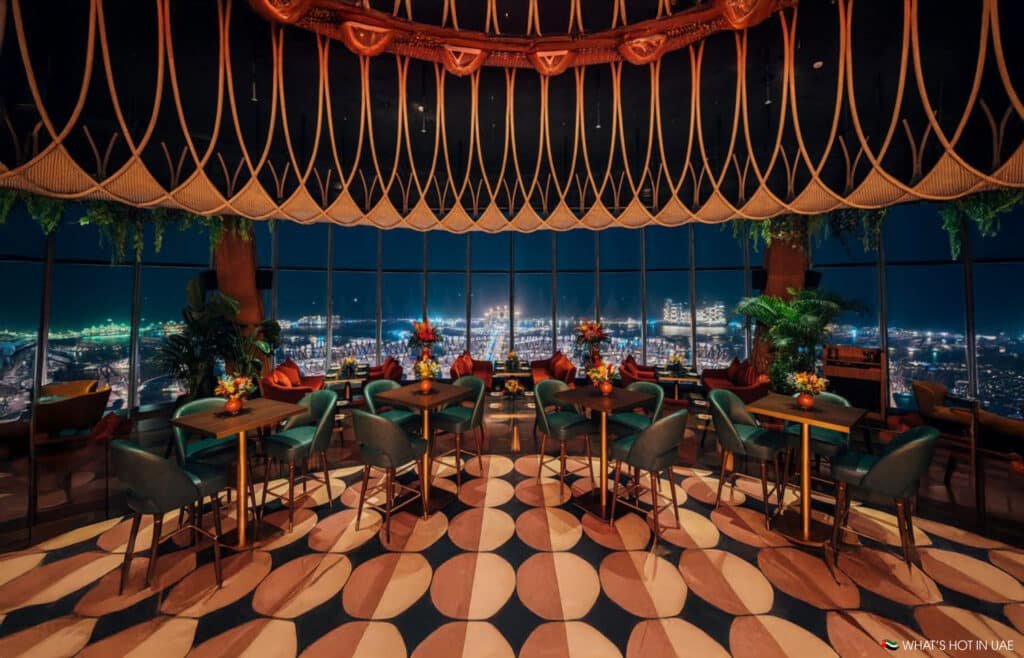 Dubai's Best Fine Dining:  stylish, upscale restaurant interior with geometric floor pattern, lush plants, and panoramic city skyline views at night.