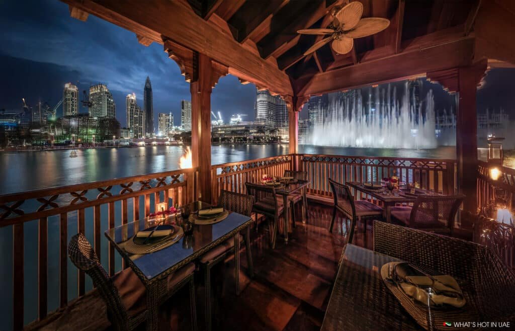 Outdoor Dubai's Best Fine Dining area overlooking a city skyline and fountain show at night, with tables set for dinner under a wooden pergola.