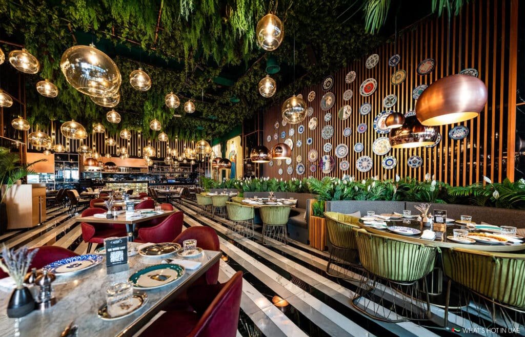 A stylish restaurant interior with vibrant decor, featuring hanging plants, modern light fixtures, and tables set for dining.