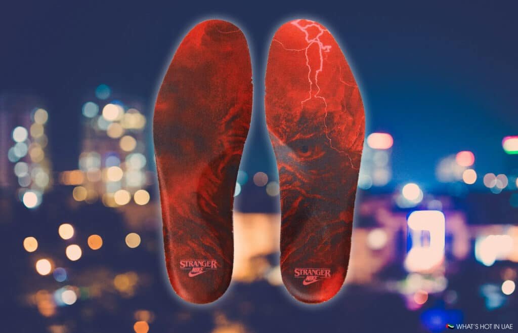Two red insoles with a dark, detailed design and text "Stranger" displayed against a blurred cityscape background.