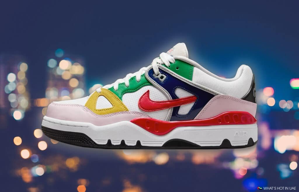Colorful sneaker with a mix of green, yellow, pink, and blue panels, featuring a prominent red Nike swoosh, against a blurred cityscape.