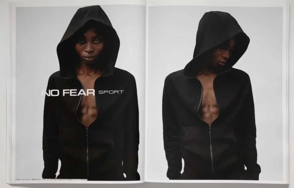 A person wearing a black NO FEAR SPORT Essentials hoodie with the text "No Fear Sport" beside them, set against a plain background.