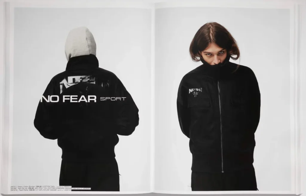 A person wears a black hoodie with "NO FEAR SPORT" printed on the back and stands with arms crossed, looking directly at the camera.