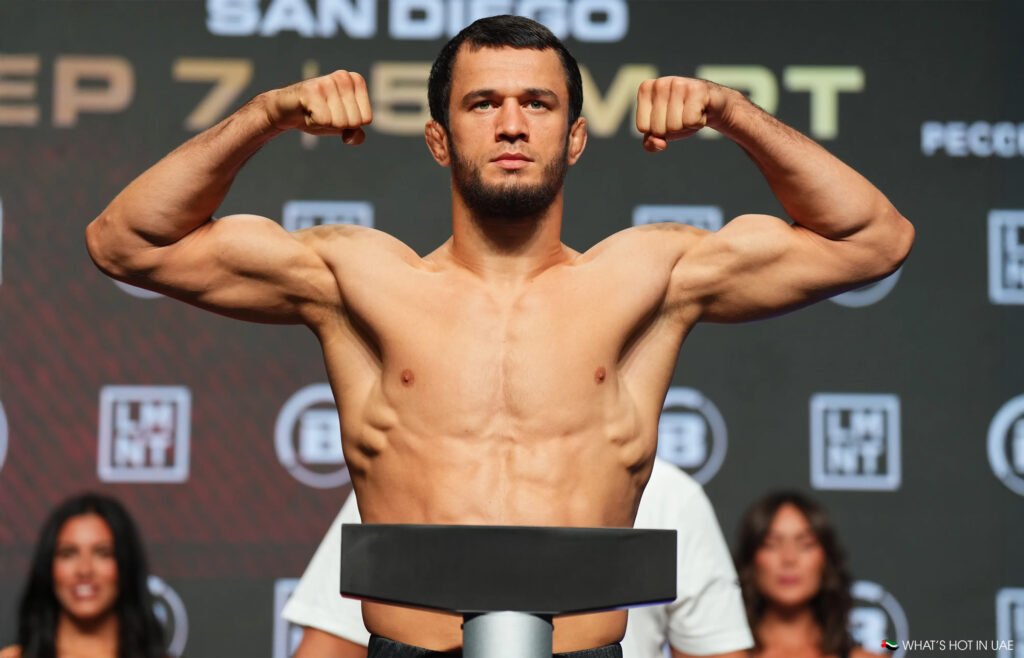 Nurmagomedov is posing with his fists raised on a stage, in front of a Nurmagomedov vs Davis backdrop with text, showcasing a muscular physique.