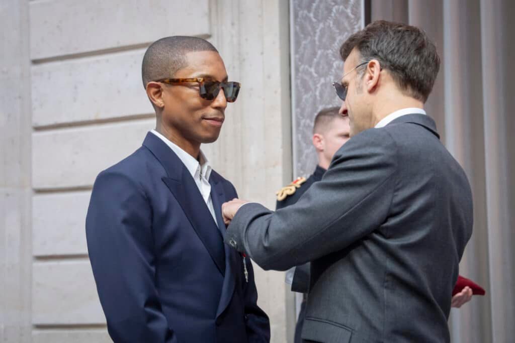 Pharrell Williams' Légion d'honneur in a suit receives a medal from another person in a formal setting.
