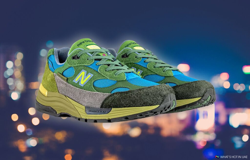 A pair of colorful sneakers with green, blue, and gray tones, featuring the letter "N" on the side, against a blurred city lights background.